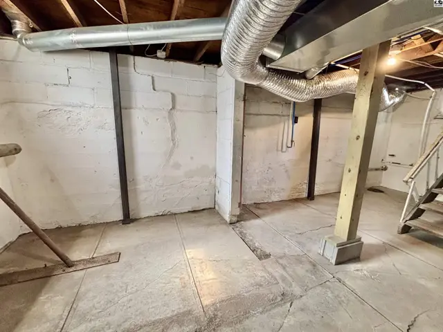 Concrete foundation walls and floor with exposed ductwork and wooden support beams.