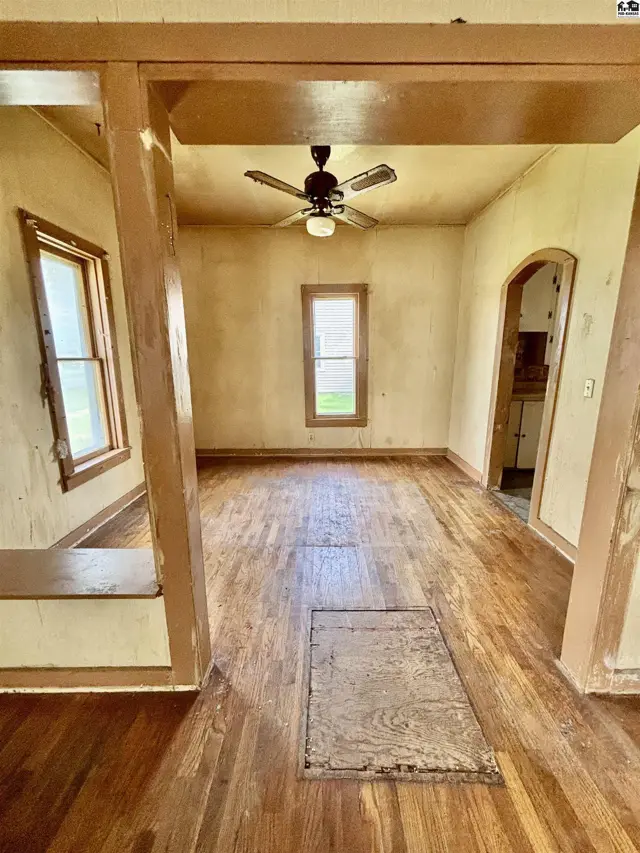 Living room with hardwood floors, ceiling fan, and arched doorway leading to kitchen.