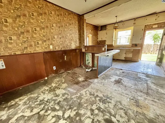 Kitchen with patterned wallpaper, wood paneling, and a central island, awaiting renovation.