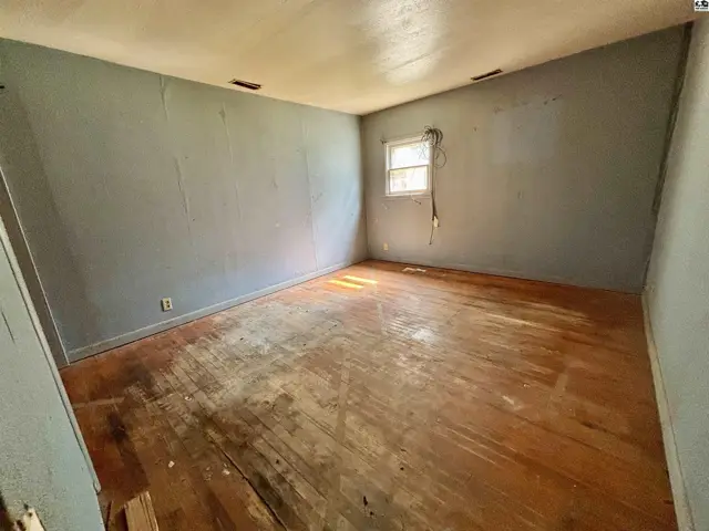 Empty bedroom with light blue walls, a small window, and distressed hardwood floors.