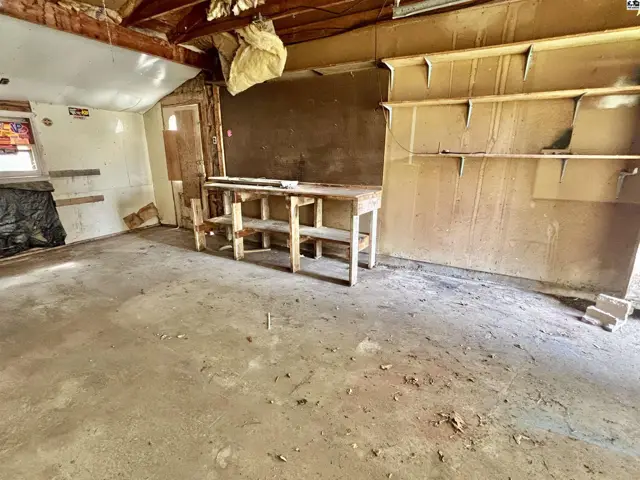 Interior of a workshop with concrete floors, wooden workbench, and unfinished walls.