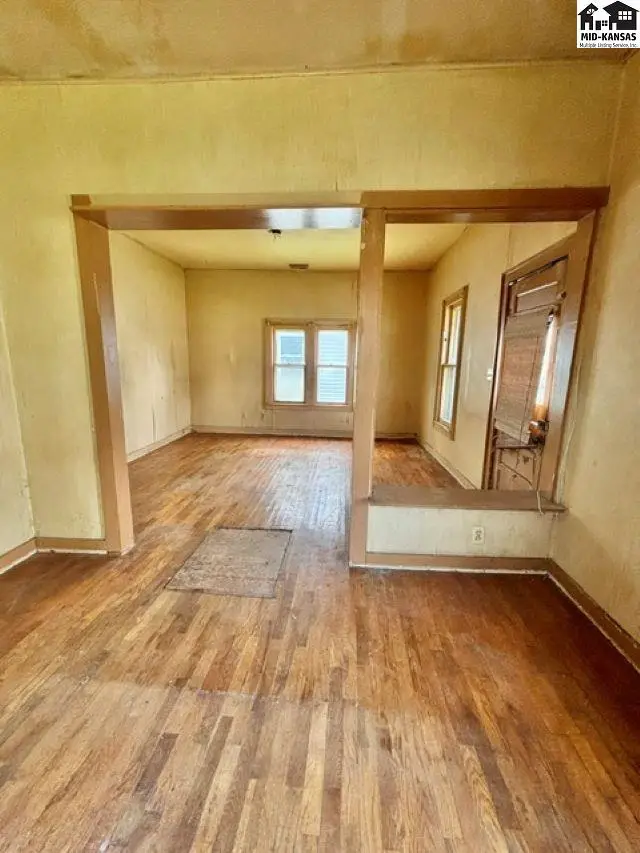 Living room with hardwood floors, light yellow walls, and a doorway to another room.