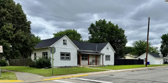 White single-story house with dark roof, featuring a covered porch and tidy lawn.