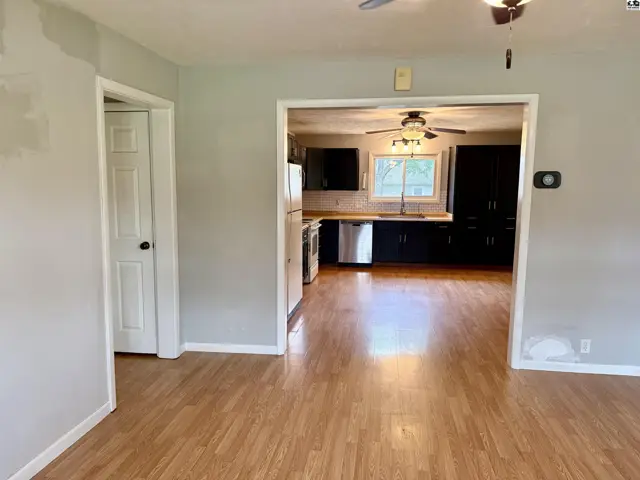 View into a modern kitchen with dark cabinets, stainless steel appliances, and light wood flooring.
