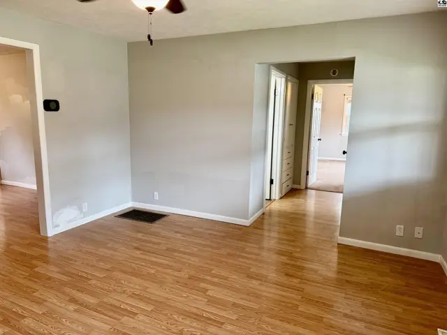 Light-filled living room with light wood laminate flooring and neutral walls, opening to hallways.