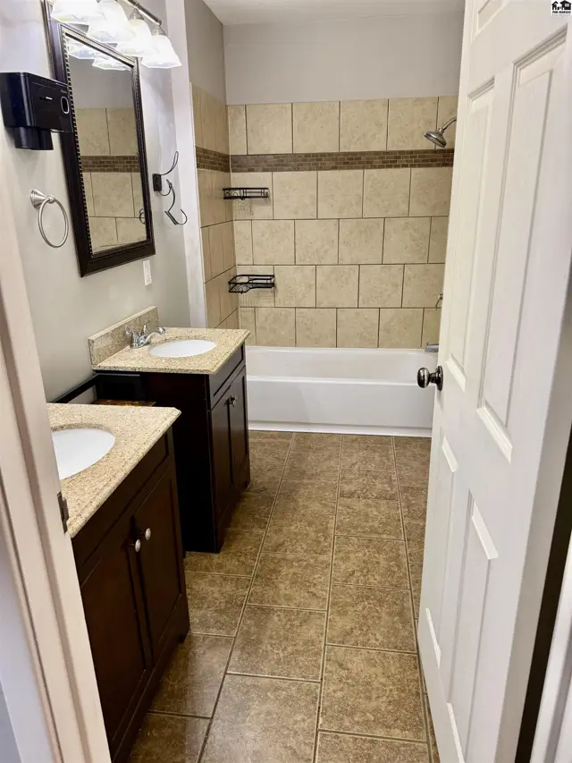 Spacious bathroom features dual vanities with granite tops, tiled shower, and warm-toned tile flooring.