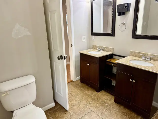 Spacious bathroom with dual vanities, granite countertops, dark wood cabinets, and tiled flooring.