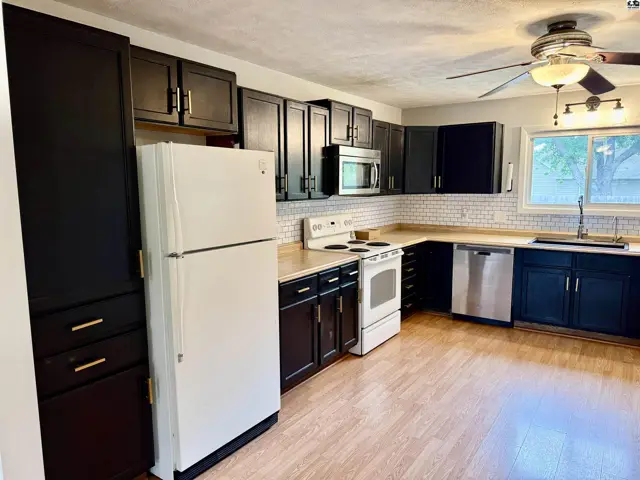 Modern kitchen with dark cabinets, white appliances, subway tile backsplash, and light wood flooring.