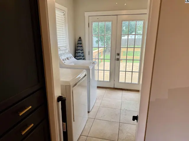 Laundry room with white appliances, tiled floor, and double doors leading to a wooden deck.