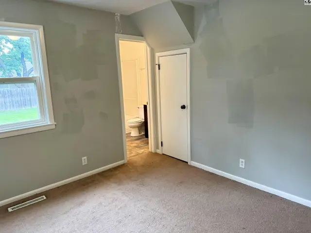 Bedroom with neutral carpet, light gray walls, and a view into a bathroom with a toilet.