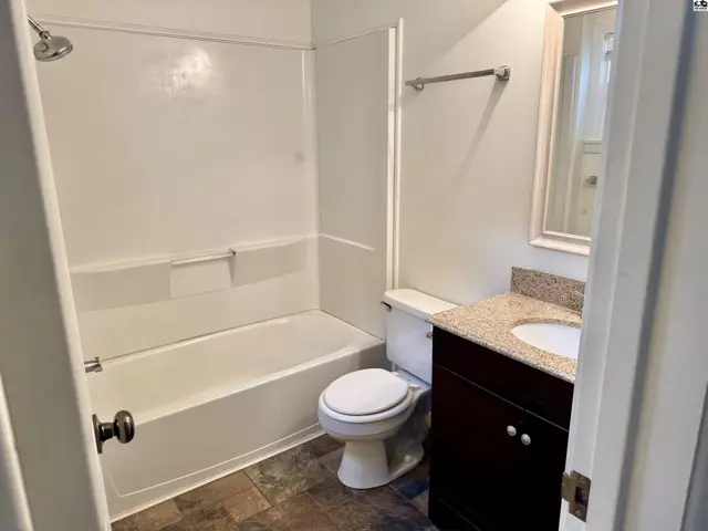 Bright bathroom features a white tub/shower combo, granite vanity, and dark wood cabinet.
