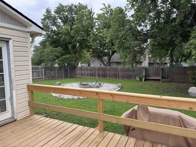 Wooden deck overlooks a fenced backyard with a circular fire pit and mature trees.