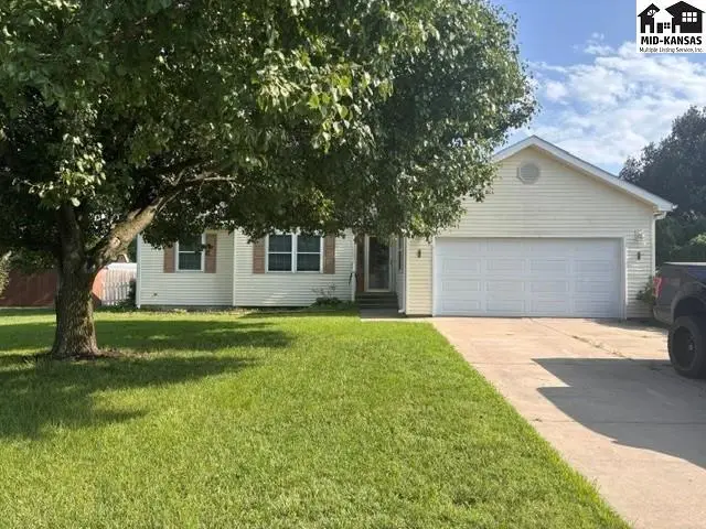 Exterior view of a light yellow vinyl-sided house with a large garage door and mature tree.