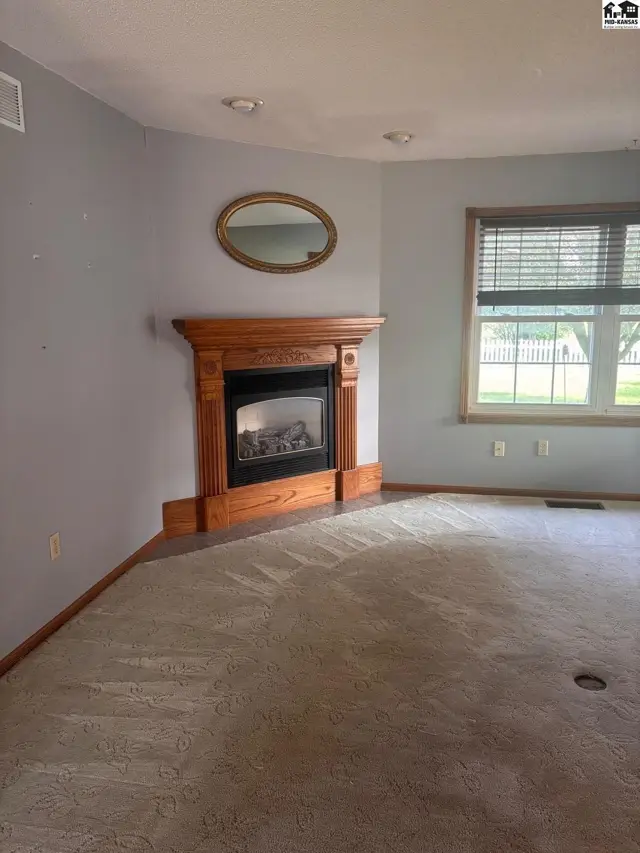 Corner gas fireplace with wood mantel, oval mirror, and plush carpet in a light blue room.