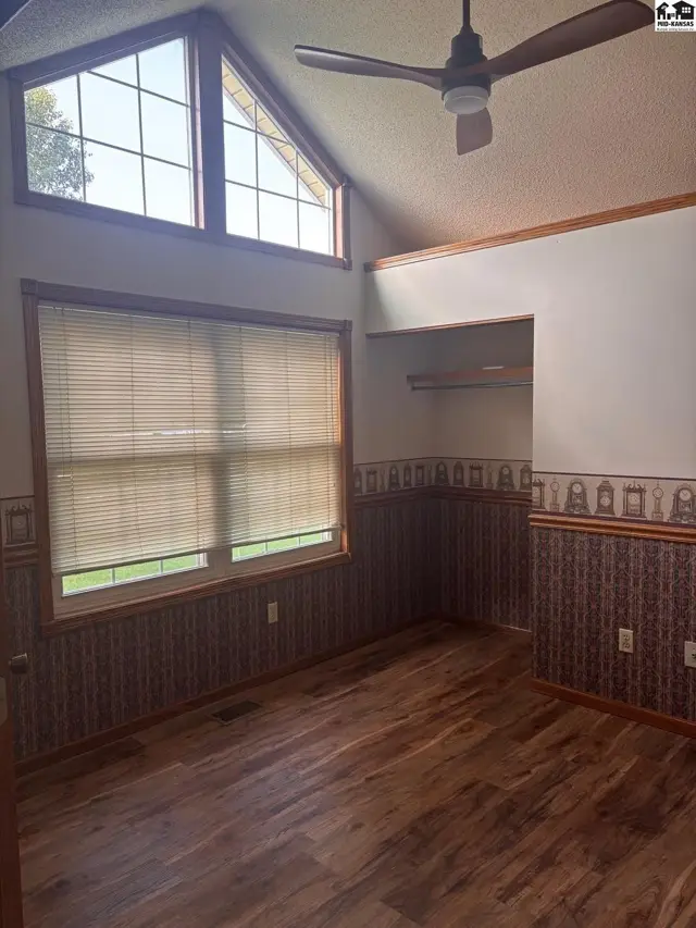 Spacious bedroom with vaulted ceiling, large windows, wood-look flooring, and patterned wallpaper.
