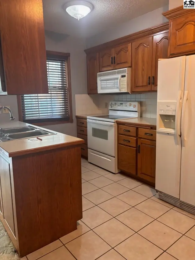 Kitchen with warm wood cabinets, white appliances, tiled floor, and light countertops.