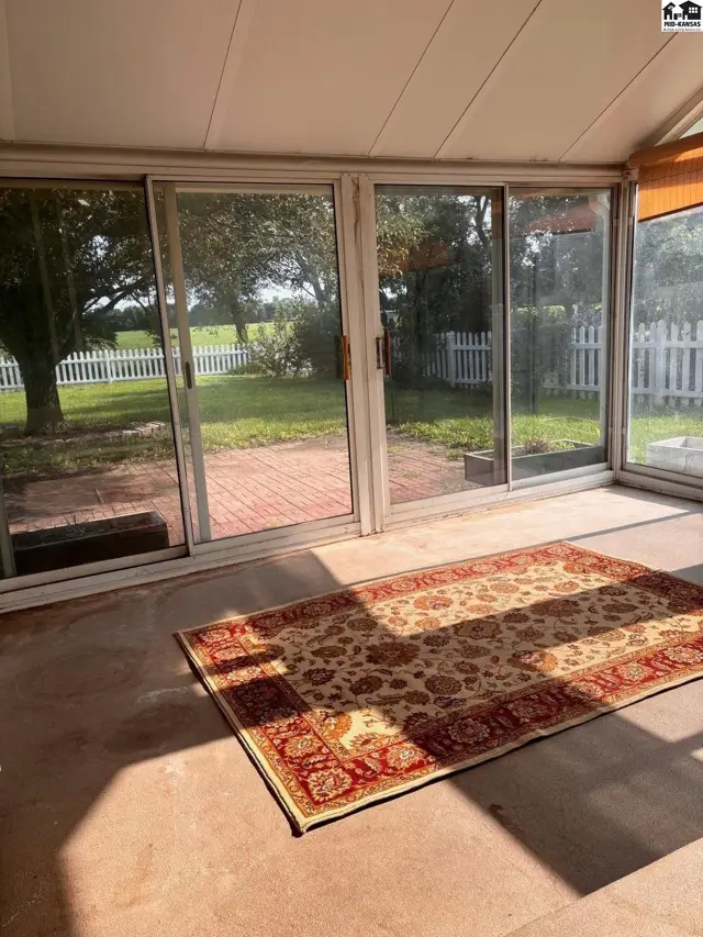 Sunroom with sliding glass doors, patterned rug, and view of a white picket fence.