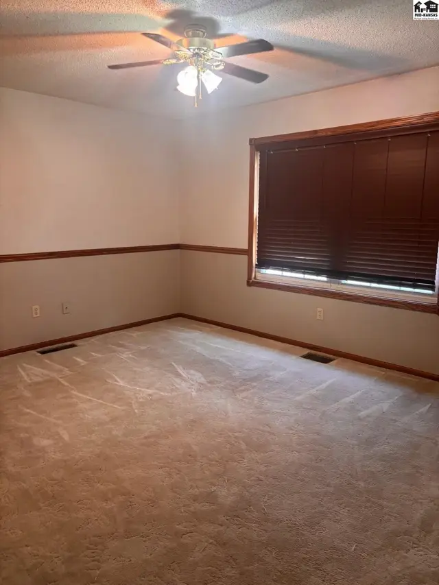 Spacious bedroom with plush carpet, two-tone walls, wood trim, and a ceiling fan.