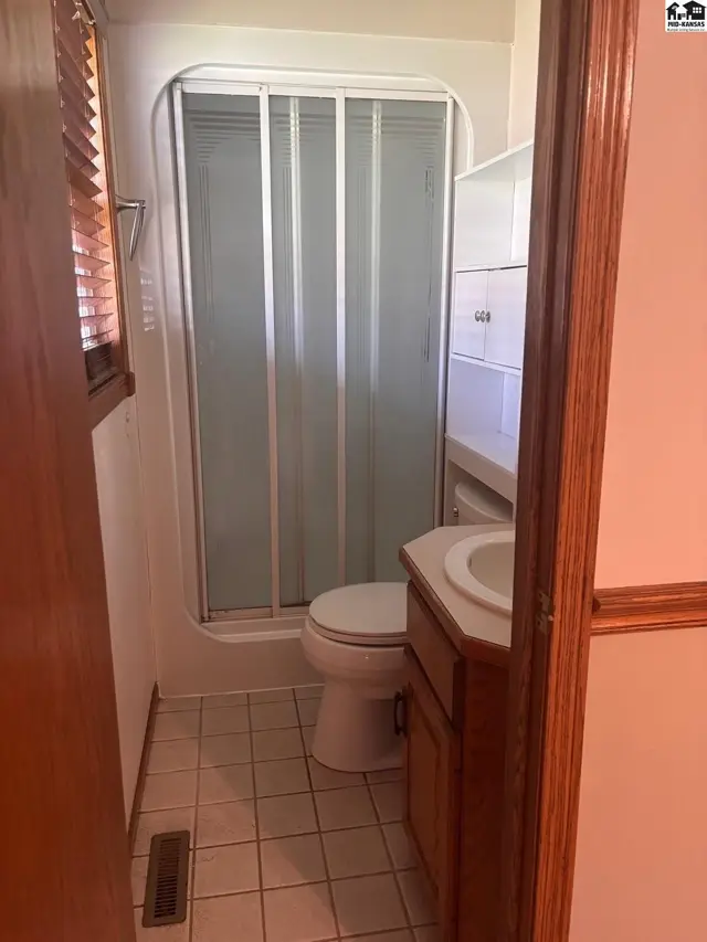 Compact bathroom with a white toilet, frosted glass shower doors, and a wooden vanity with a beige countertop.