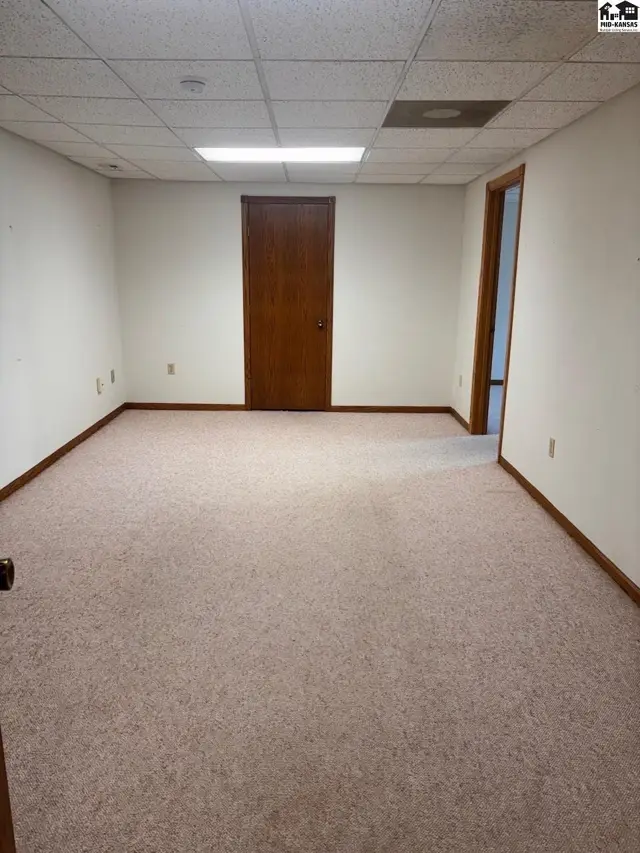 Spacious room with plush carpet, white walls, and a wood-paneled door.