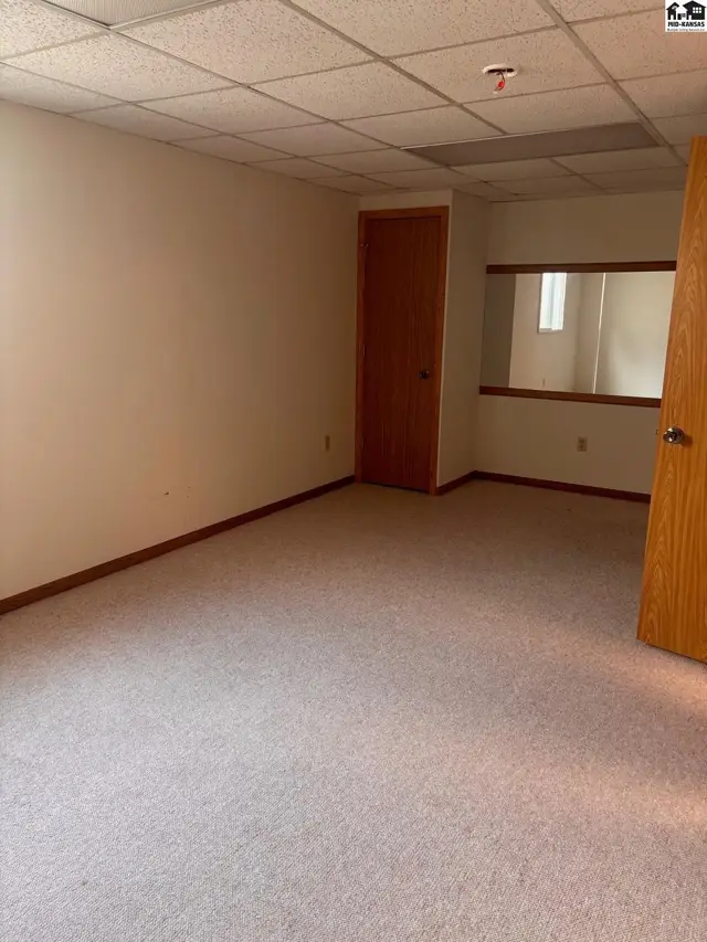 Carpeted room with wood doors, beige walls, and a mirrored partition.