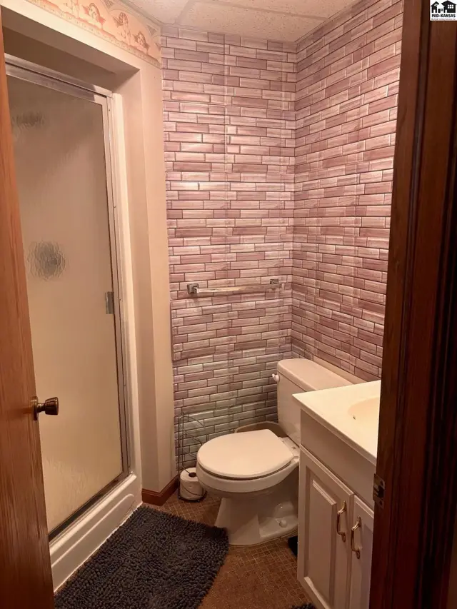 Bathroom with a glass-enclosed shower, white vanity, and faux brick wallpaper.