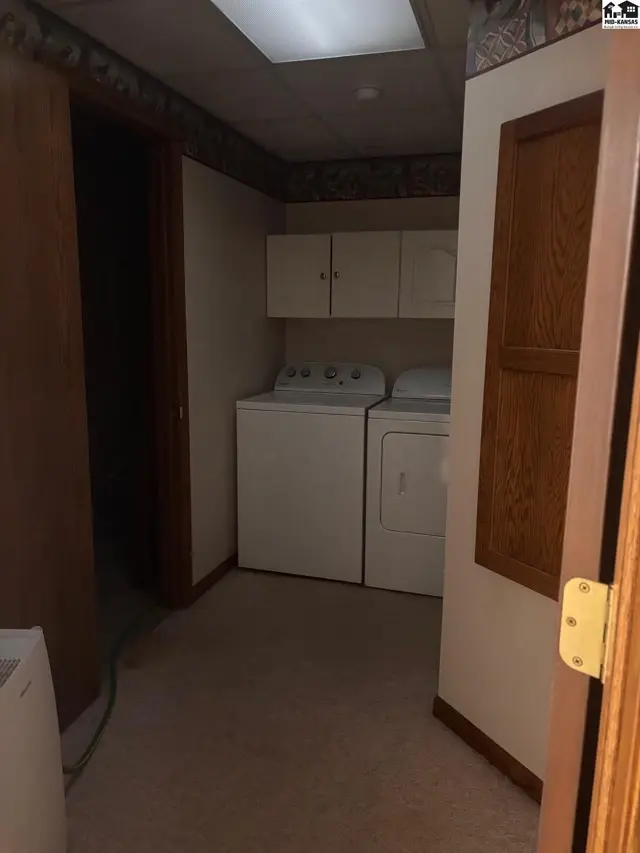 Laundry room with white washer and dryer, beige carpet, and wood-paneled door.