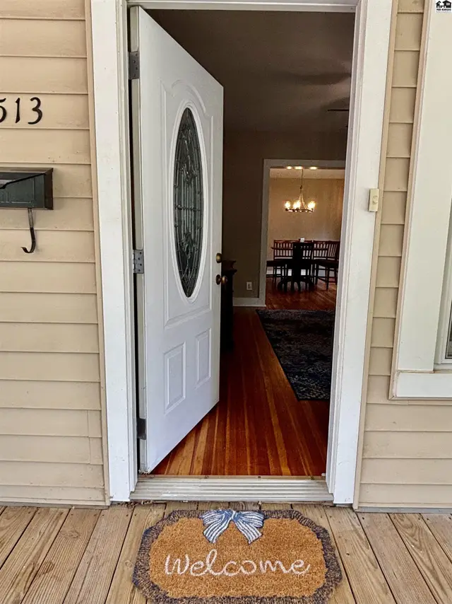 Open front door reveals a welcoming entryway with hardwood floors and a glimpse of the dining room.