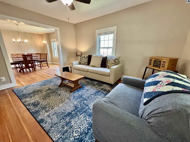 Living room with neutral walls, hardwood floors, a patterned rug, and a view into the dining area.