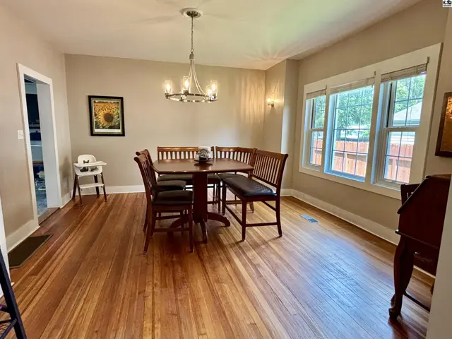 Warm dining room with wood floors, a round table with chairs and bench, and large windows.