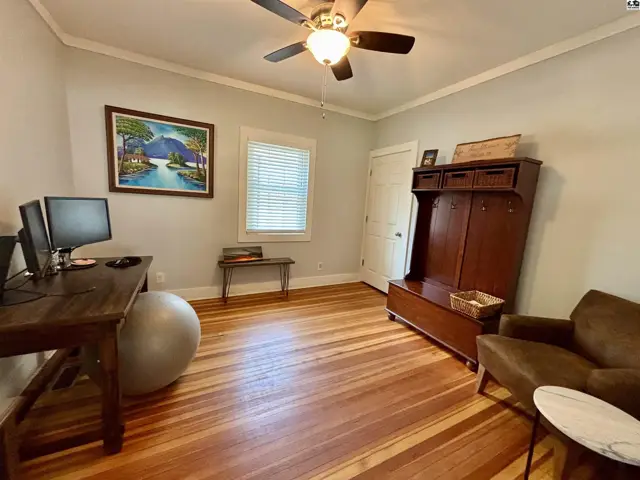 Spacious room with hardwood floors, a desk with computers, a large exercise ball, and a tall wooden cabinet.