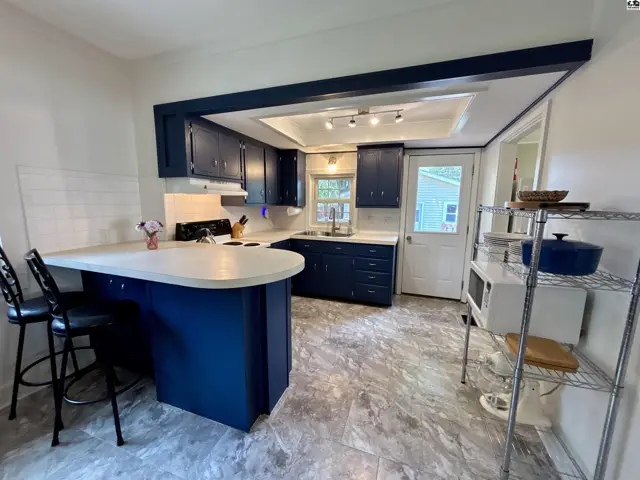 Modern kitchen with navy cabinets, white countertops, and gray tile flooring, featuring a breakfast bar.