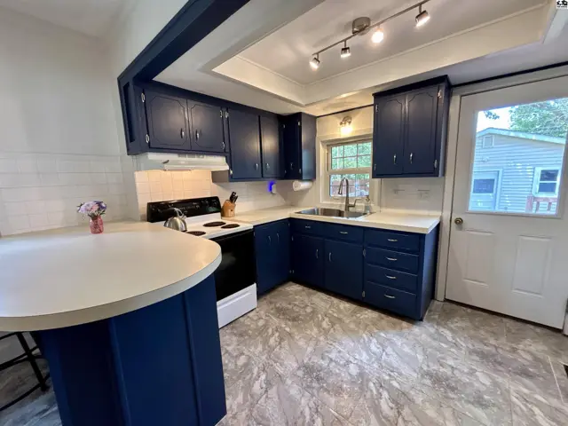 Navy blue cabinets and a white island complement the modern kitchen with white subway tile and gray flooring.