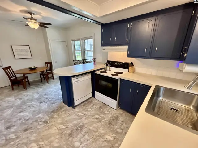 Kitchen with navy cabinets, white countertops, stainless steel sink, and adjacent dining area.