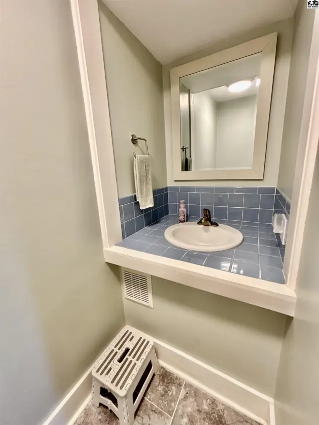 Powder room with a white pedestal sink, blue tiled backsplash, and a white step stool.