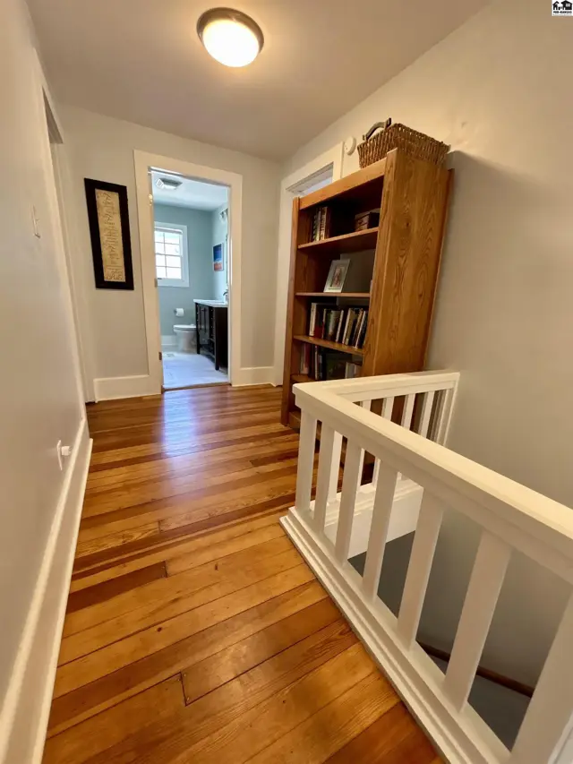 Hallway with gleaming hardwood floors, a wooden bookshelf, and a view into a light-filled bathroom.
