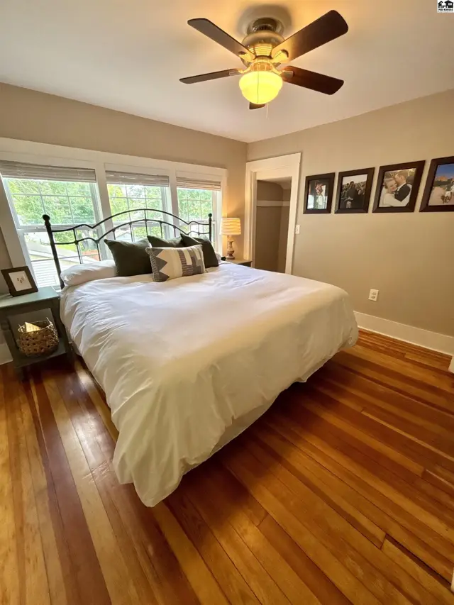 Spacious bedroom with a wrought-iron bed, hardwood floors, and large windows.