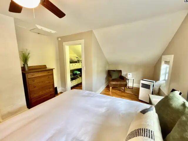 Cozy bedroom with sloped ceilings, hardwood floors, a dresser, and an open closet.