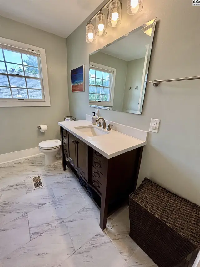Modern bathroom with dark wood vanity, white quartz countertop, marble tile floor, and large beveled mirror.