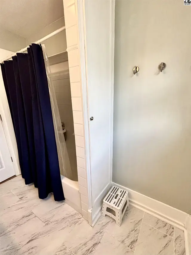 Modern bathroom with marble-look tile floors, white subway tile shower surround, and a navy blue shower curtain.