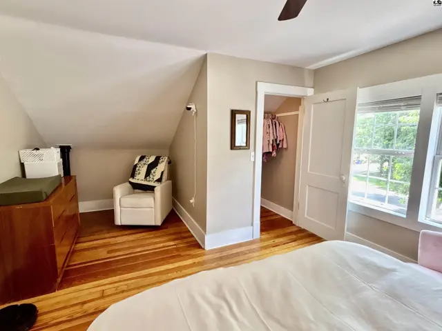 Attic bedroom with sloped ceilings, hardwood floors, a white armchair, and a walk-in closet.