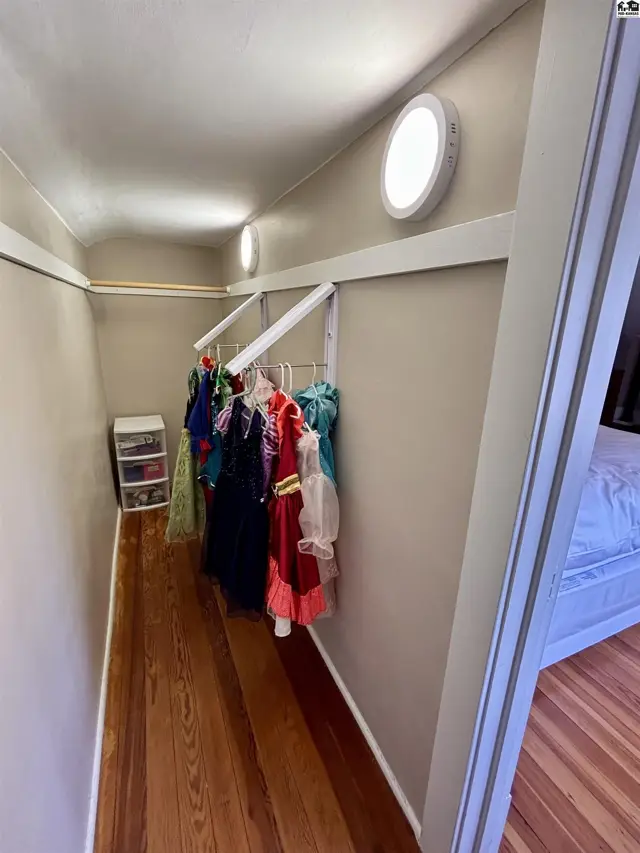 Walk-in closet with wooden floors, white shelving, and a rack of colorful dresses.