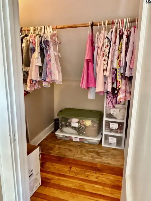 A well-organized closet with a wooden floor, featuring children's clothing on hangers and storage bins.