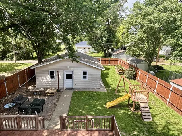 Backyard with a wooden deck, swing set, and a small, light-colored house.