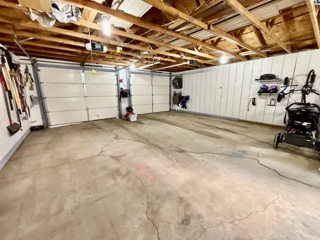 Spacious two-car garage with white paneled walls, concrete floor, and exposed wooden ceiling beams.