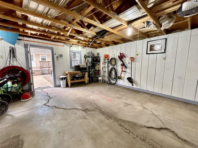 Spacious garage with concrete floor, white paneled walls, and exposed wooden ceiling beams.