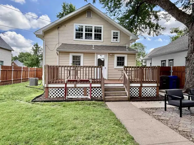 Exterior view of a beige vinyl-sided house with a wooden deck and patio.