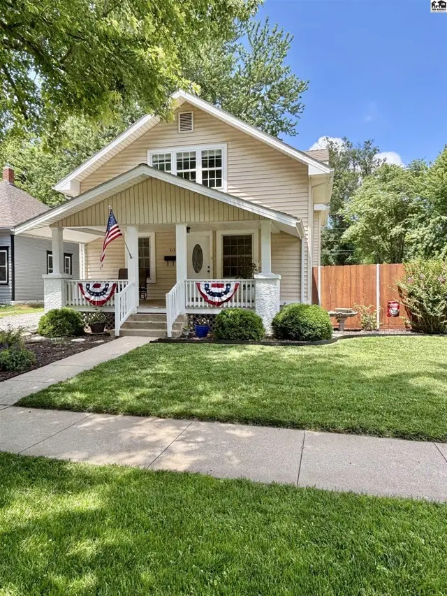 Charming beige bungalow with white trim, a covered porch, and patriotic decorations.