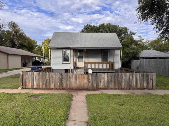 Exterior of a light blue house with a wooden fence, porch, and mature trees.