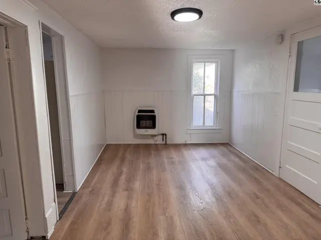 Bright room with wood-look flooring, white wainscoting, and a wall-mounted heater.